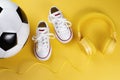 Close-up photo of yellow headphones, white sneakers and traditional style soccer ball over yellow background. Royalty Free Stock Photo