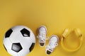 Close-up photo of yellow headphones, white sneakers and traditional style soccer ball over yellow background. Royalty Free Stock Photo