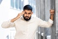 Close-up photo of a young Arab man in a shirt and jeans standing outside with his eyes closed, leaning against the wall Royalty Free Stock Photo