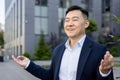 Close-up photo of young Asian male businessman sitting relaxed outside working office in lotus yoga pose and meditating Royalty Free Stock Photo