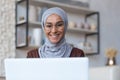 Close-up photo of young beautiful Arab woman in hijab and glasses working at home sitting in kitchen smiling and happy Royalty Free Stock Photo