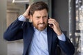 Close-up photo of a young businessman man in a suit standing in an office center, worriedly talking on the phone and Royalty Free Stock Photo