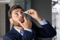 Close-up photo of a young businessman sitting in the office at a desk in a suit and instilling medicine into his eye