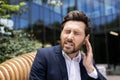 Close-up photo of a young businessman writhing in pain, sitting on a bench near the office and holding his hand by his Royalty Free Stock Photo