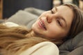 Close up photo of young cute girl, student smiling with teeth in braces lying on coach and dreaming against blurred Royalty Free Stock Photo