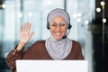 Close-up photo. Young hispanic female student in hijab sitting at desk in office wearing headset and talking on video Royalty Free Stock Photo