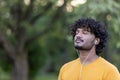 Close-up photo of a young Indian male athlete wearing headphones standing in a park listening to music and resting with Royalty Free Stock Photo