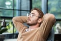 Close-up photo. Young man freelancer, student sits on a chair in the office, coffee shop and rests. He put his hands Royalty Free Stock Photo