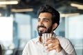 Close-up photo of a young man, an Indian businessman sitting in the office and holding a glass of clean water in his Royalty Free Stock Photo