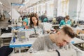 photo of a young man and other seamstresses sewing with sewing machine in a factory