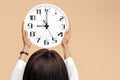 Close-up photo of young modern business woman hold a clock over head on beige background. Royalty Free Stock Photo