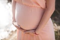 Close up photo of young pregnant woman in elegant pink dress touching her belly with hands. Royalty Free Stock Photo