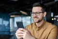 Close-up photo. Young smiling male businessman sitting with phone in office, calling, texting, chatting, searching and Royalty Free Stock Photo