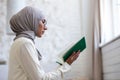Close-up photo. A young woman in a hijab and glasses, holding a green holy book in her hands, folded her hands and prays Royalty Free Stock Photo