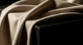 Close-up of smooth beige silk fabric elegantly draped over a black rectangular box against a dark minimalist background Royalty Free Stock Photo