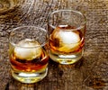 Two cocktail glasses with an amber alcoholic beverage, Rusty Nail, and round ice cubes on a rustic barn wood background. Royalty Free Stock Photo