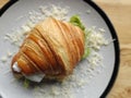 Close-up photography of a crispy croissant sandwich filled with lettuce leaf, tomato, and white cheese on a white plate. Royalty Free Stock Photo