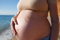 Heart of sand on the belly of a pregnant woman against the background of the sea
