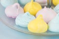 Close up photography of a small blue, yellow and pink meringues served in a crystal plate on a pale blue surface. Sweet snack