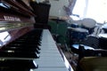 Close up of piano keyboard with drum kit in background of a music room