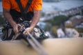 Close up pic of male rope access job industrial worker, using a safety device descender on static twin ropes abseiling, repairing