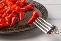 Close-up of pickled red hot pepper on a fork against black plate. Spicy appetizer of fermented organic vegetables. Marinated pods Royalty Free Stock Photo