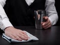 Close-up of a bartender cleaning a bar counter. Barkeeper with a shaker and a white handkerchief on a black background.