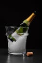 An expensive bottle of champagne in a transparent bucket filled with ice on a black background. Celebration concept.