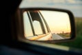 Close-up picture of car side mirror with beautiful road view with blue yellow sky at sunset. Auto traveling. Summer vacation road Royalty Free Stock Photo