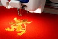 Close up picture of embroidery machine and gold lion logo on the red fabric