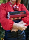 Close-up picture of hands, holding a bunch of books and red apple. Female student, wearing red shirt and black skirt, with many