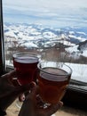 Close-up picture of two glasses with hot tea, held in hands of man and woman, near window with beautiful mountain view. Ski resort Royalty Free Stock Photo