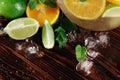 Close-up of a new citrus drink preparation. Green lime, mint and juicy orange with crushed ice on a wooden background.