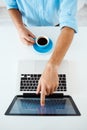 Close up picture of young businessman's hands sitting at table pointing on laptop screen holding coffee cup. White