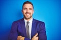Close up picture of young handsome business man over blue isolated background happy face smiling with crossed arms looking at the Royalty Free Stock Photo