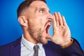 Close up picture of young handsome business man over blue isolated background shouting and screaming loud to side with hand on