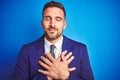 Close up picture of young handsome business man over blue isolated background smiling with hands on chest with closed eyes and Royalty Free Stock Photo