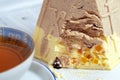 Close up piece of pastry or confectionery, layered, with candied fruit, cup of tea near. Royalty Free Stock Photo