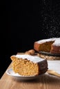 Close-up of piece of sponge cake with sugar on wooden table with spoon, in the background carrot sponge cake defocused, falling su