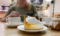 Close-up of piece transparent gelatin cake with meringue cream on the table in cafe with blond girl