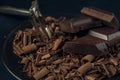 Close-up pieces of chocolate, chocolate shavings and peeler in black plate on dark textured background