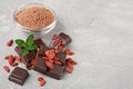 Close-up pieces of dark chocolate bar with dried Goji berries, glass bowl of cocoa powder and mint