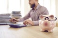 Close up of piggy bank in form of pink pig with glasses standing on table on background of busy man. Royalty Free Stock Photo