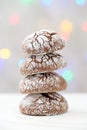 Close up of a pile of four crackled cocoa cookies, arranged like a snowy Christmas tree, against blurred, colorful Christmas