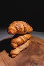 Close-up of a pile of three croissants on a wooden board against a dark background. Delicious and healthy breakfast