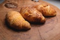 Close-up of a pile of three croissants on a wooden board against a dark background. Delicious and healthy breakfast