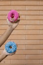 Close-up of a pink doughnut with red cherry and sprinkle glaze and a blue donut with beads held by a man`s hands