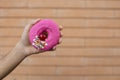 Close-up of a pink doughnut with red cherry and sprinkle glaze, held by an American male hand