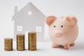 Close up of pink piggy money bank stacks of golden coins on white wall background with house. Money accumulation Royalty Free Stock Photo