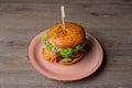 Close-up of pink plate with fresh burger with lettuce, red onion, tomato, chicken punctured with stick on wooden table.